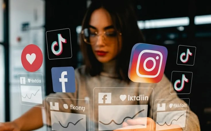 A marketer at a desk with Facebook, Instagram and TikTok icons and floating performance cards above the keyboard.